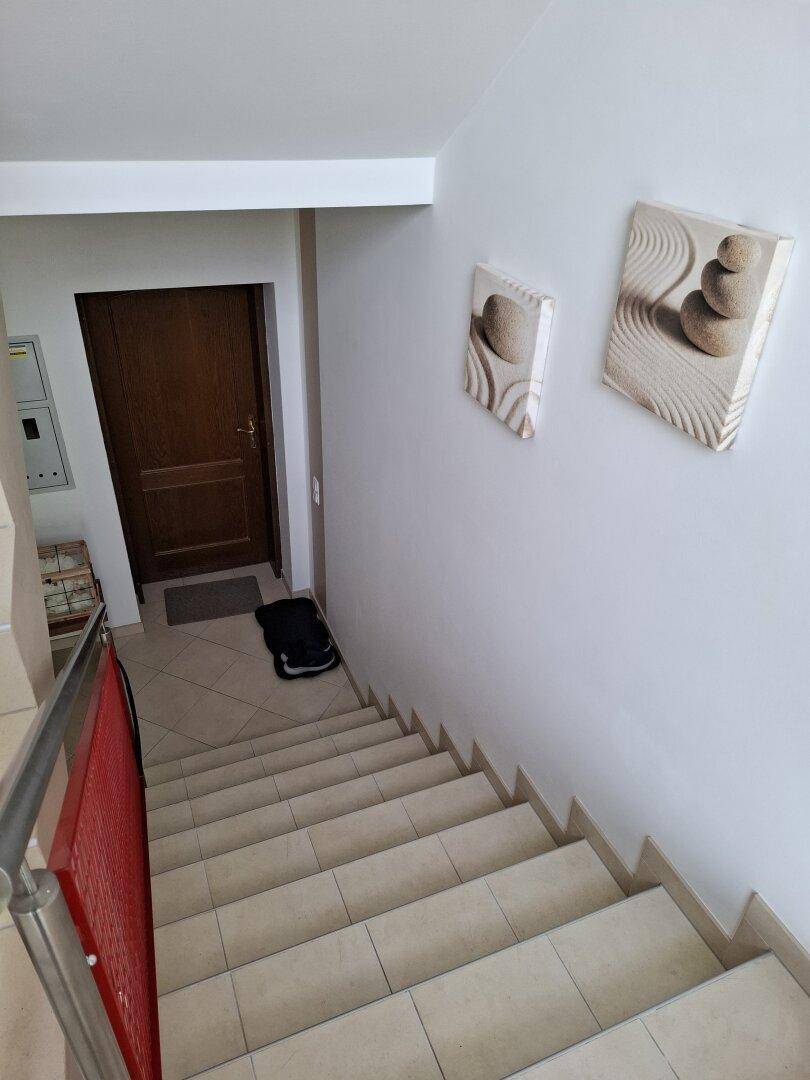 Geflieste Treppe mit Holzgeländer und einer Holztür am unteren Ende.