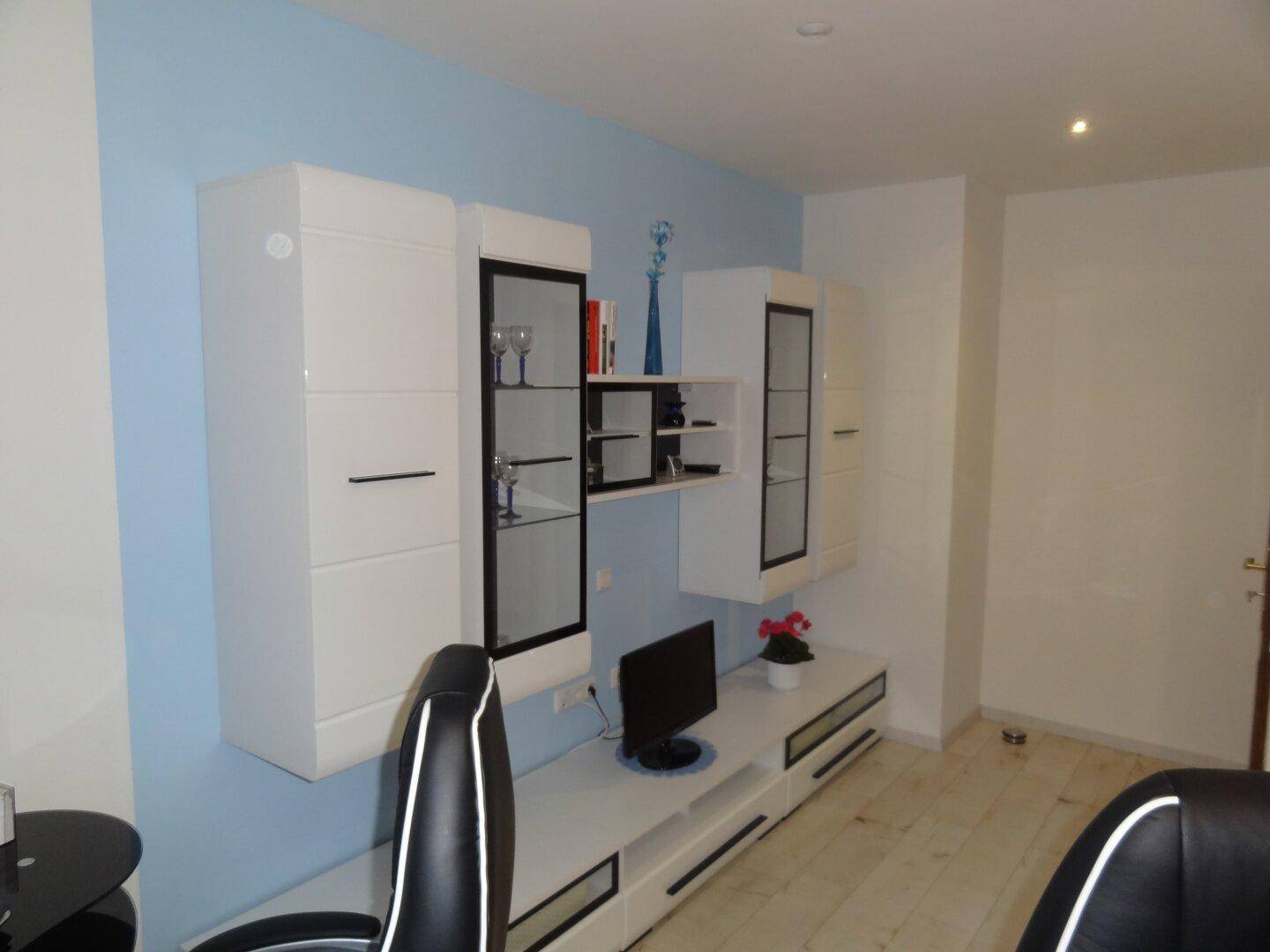 Modernes Wohnzimmer mit weißen Schränken, Fernseher und hellblauer Akzentwand.