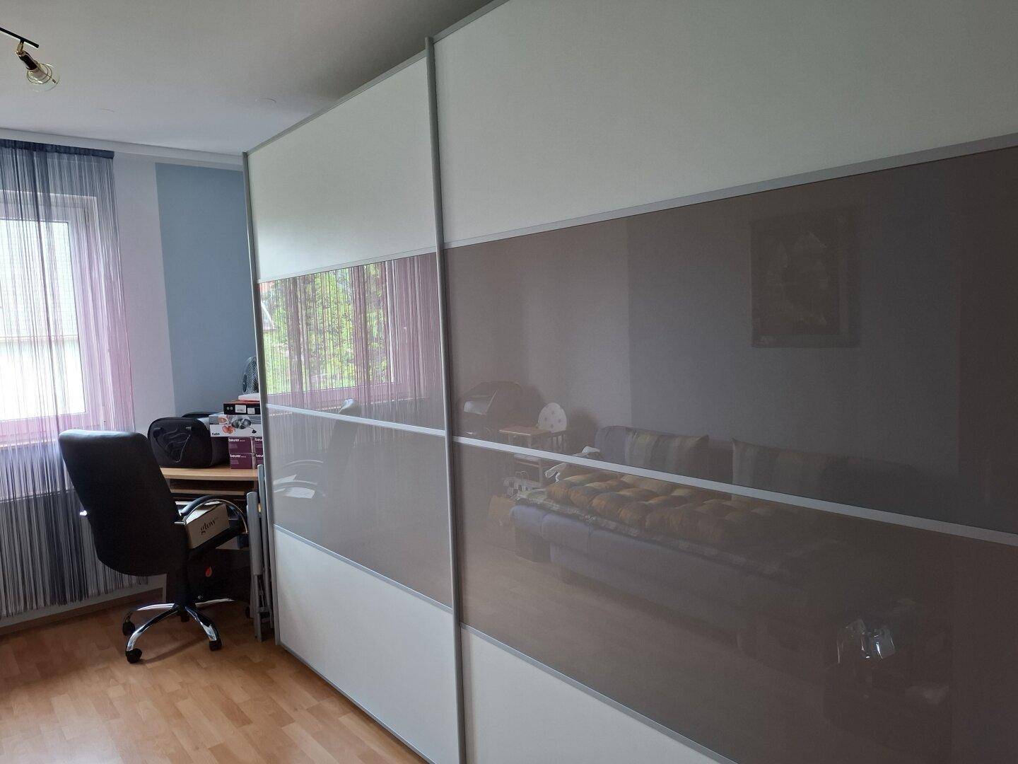 Schlafzimmer mit großem Schiebetürenschrank und Schreibtisch am Fenster.