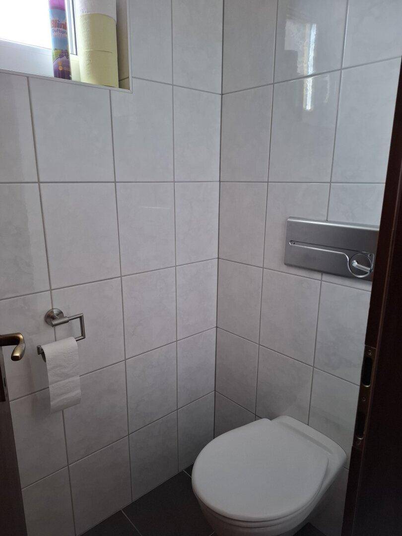 WC mit weißen Fliesen und wandhängender Toilette, hell und sauber.