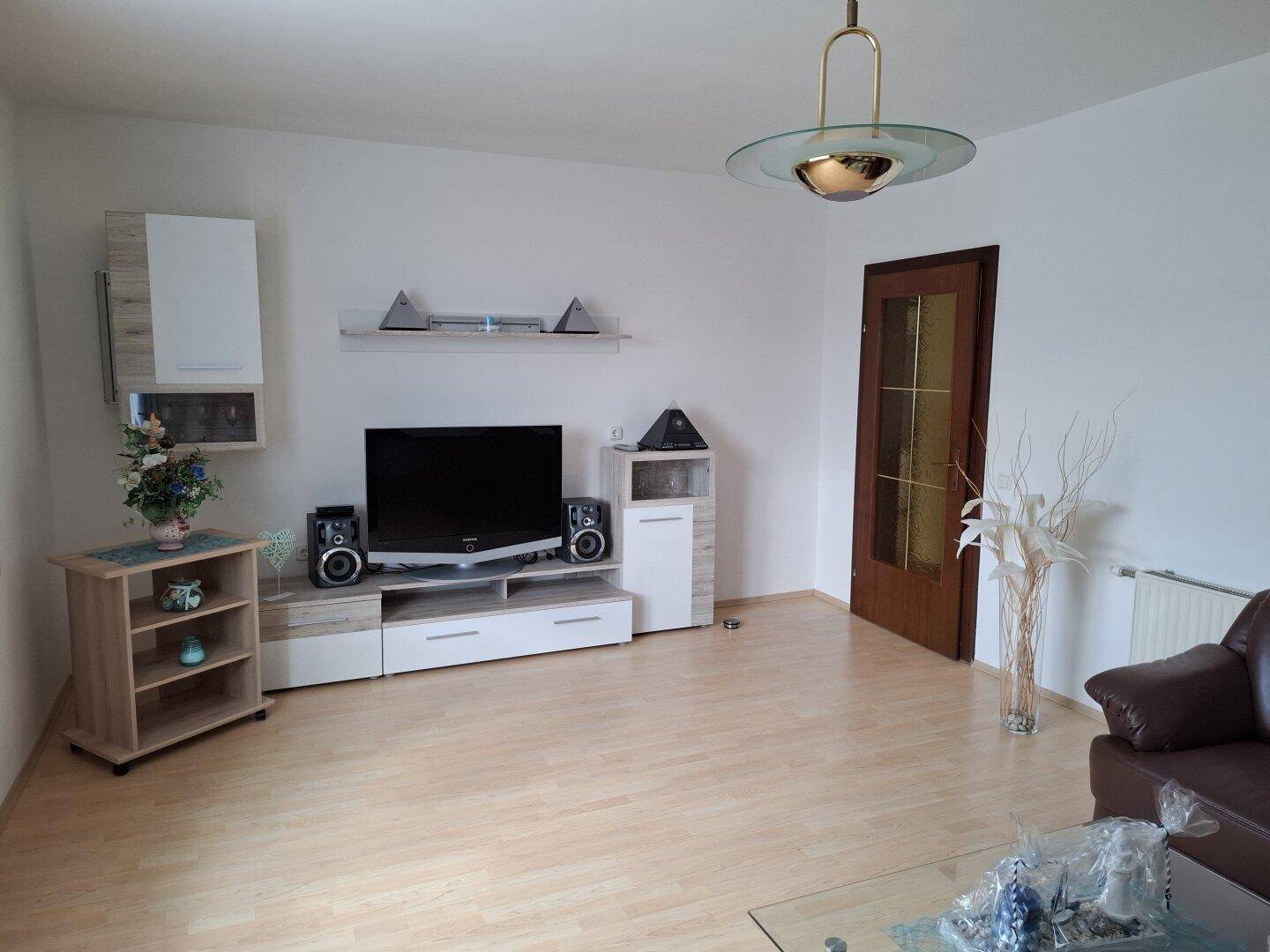 Helles Wohnzimmer mit Laminatboden, TV-Möbeln und braunem Ledersofa.