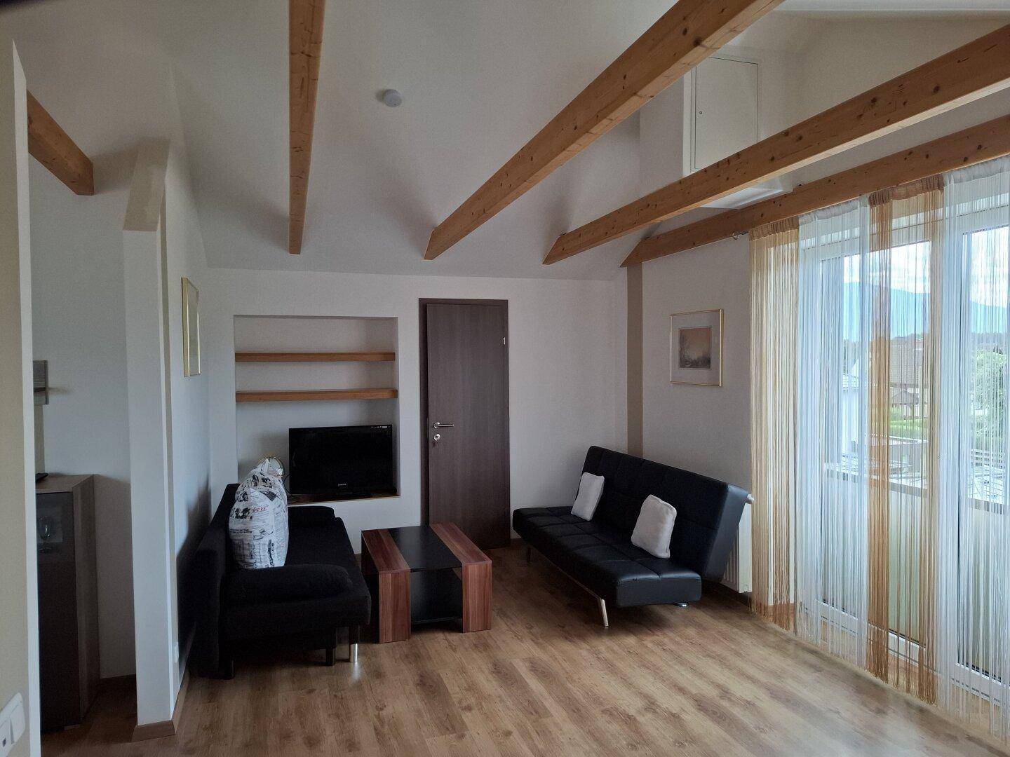 Wohnzimmer in einer Dachgeschosswohnung mit sichtbaren Holzbalken und Sofa.