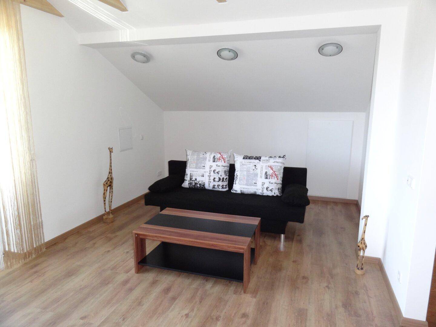 Wohnzimmer in einer Dachgeschosswohnung mit Sofa und schräger Decke.