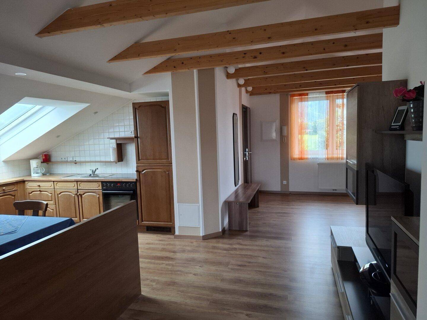 Offener Wohnbereich in einer Dachgeschosswohnung mit Küchenzeile und Holzbalken.