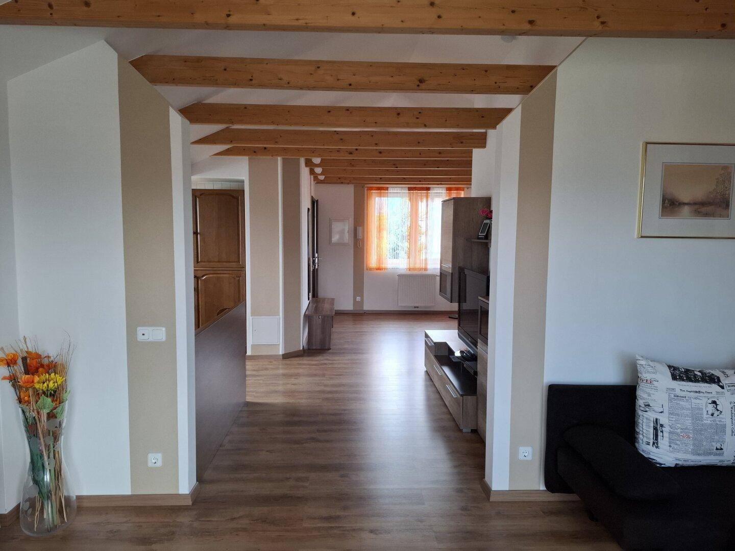 Blick durch eine offene Dachgeschosswohnung mit sichtbaren Holzbalken und viel Licht.