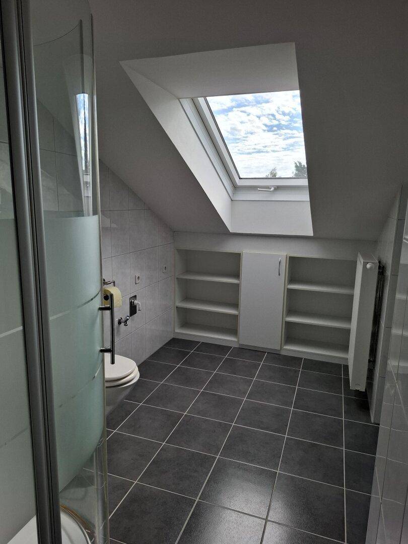 Modernes Badezimmer im Dachgeschoss mit großem Dachfenster, dunklen Bodenfliesen und Duschkabine.