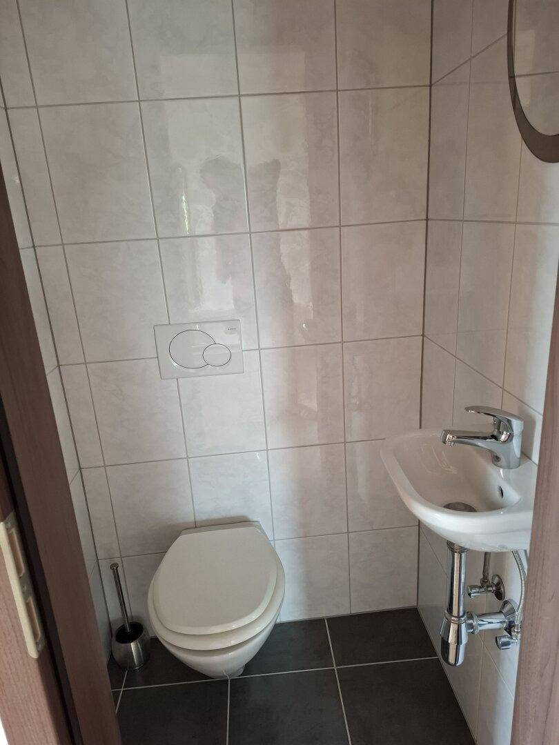 Kleines Gäste-WC mit weißen Wandfliesen, wandhängendem WC und einem kompakten Waschbecken.