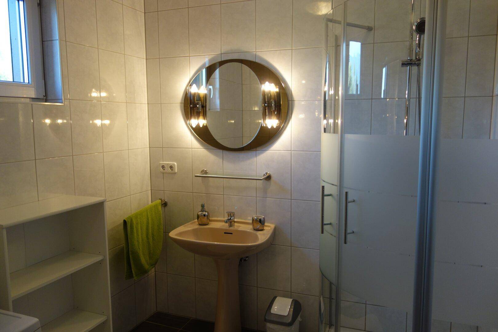 Badezimmer mit Standwaschbecken, Duschkabine und hell gefliesten Wänden.