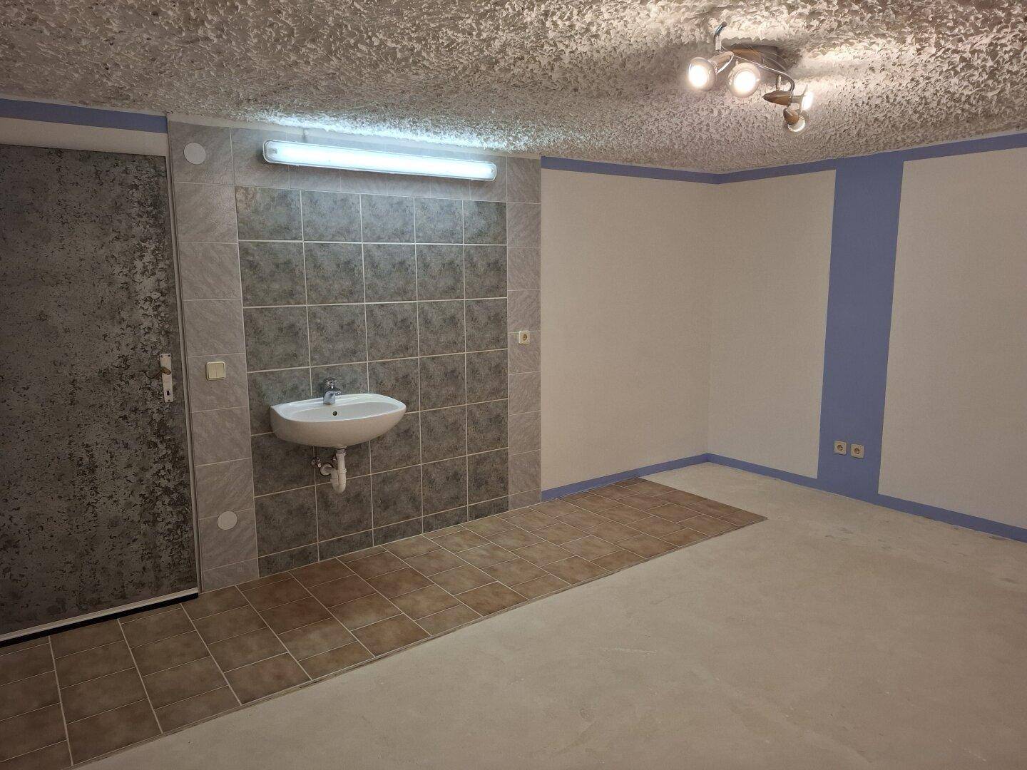 Geräumiger Abstellraum mit Waschbecken, gefliestem Bereich und strukturierter Decke.
