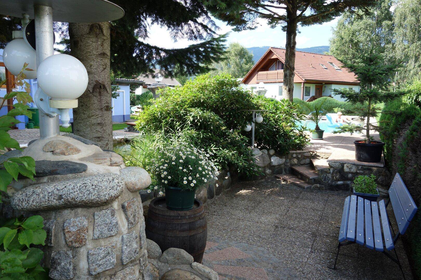 Gepflegter Gartenbereich mit Bäumen, Sträuchern, einer Steinlaterne und einer blauen Gartenbank.