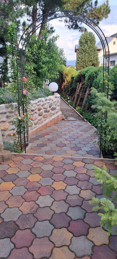 Geschwungener Gartenweg mit dekorativem Metallbogen, umgeben von üppiger Bepflanzung.