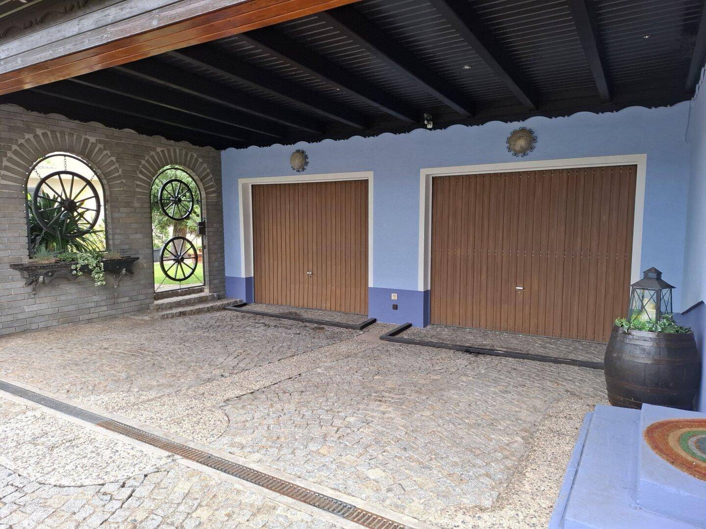 Doppelgarage mit Holztoren und gepflasterter Zufahrt, verziert mit traditionellen Elementen.