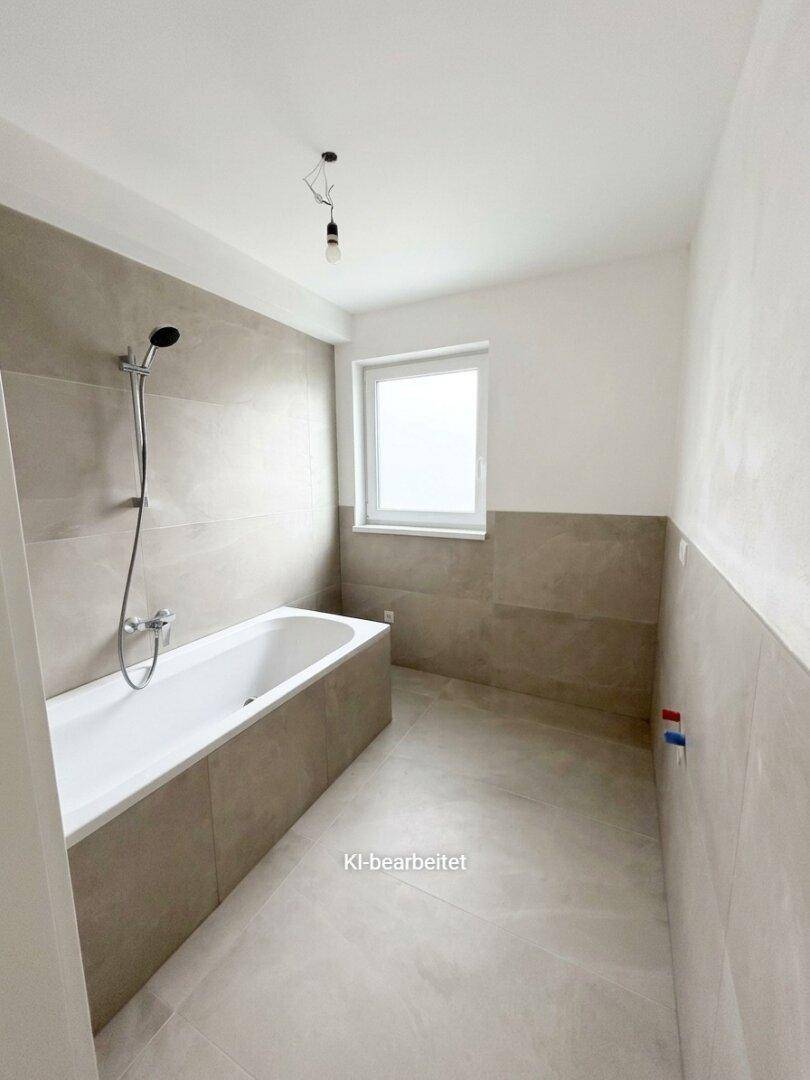 Modernes Badezimmer mit Badewanne, hellen Fliesen und Fenster für Tageslicht.