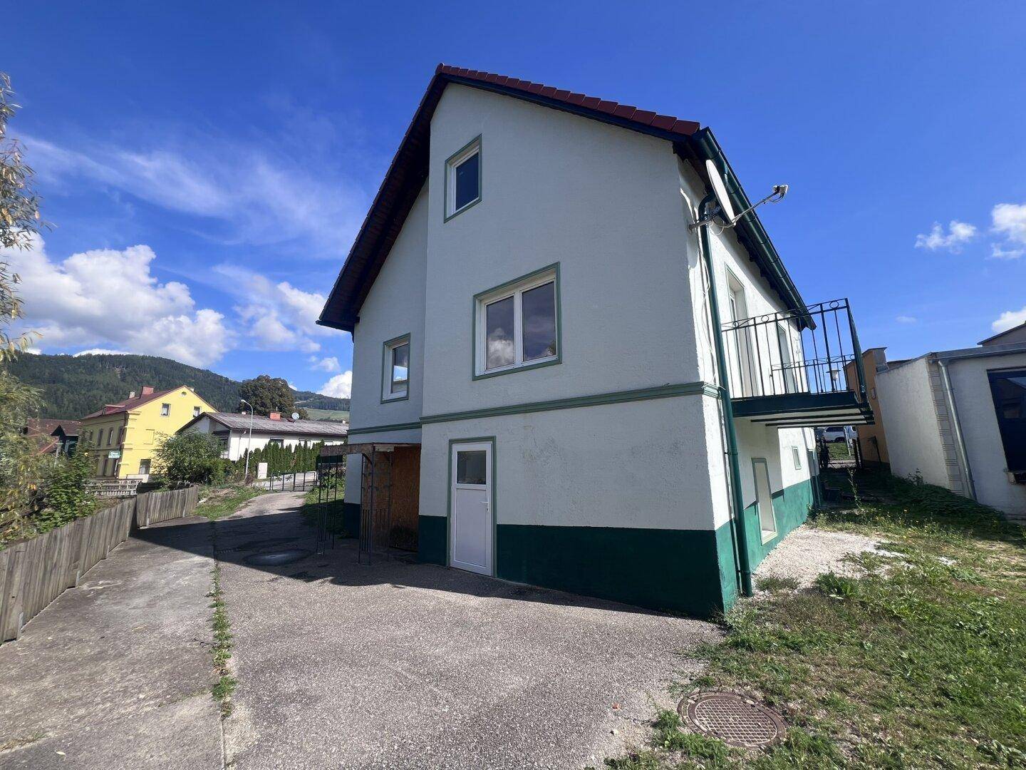 Seitenansicht des Hauses mit weißer Fassade, grünem Sockel und Zugang zum Grundstück.