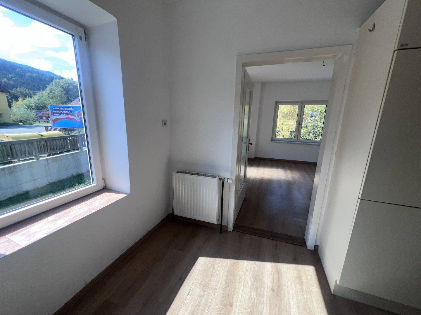 Heller Flurbereich mit Laminatboden und Blick durch ein großes Fenster ins Grüne.