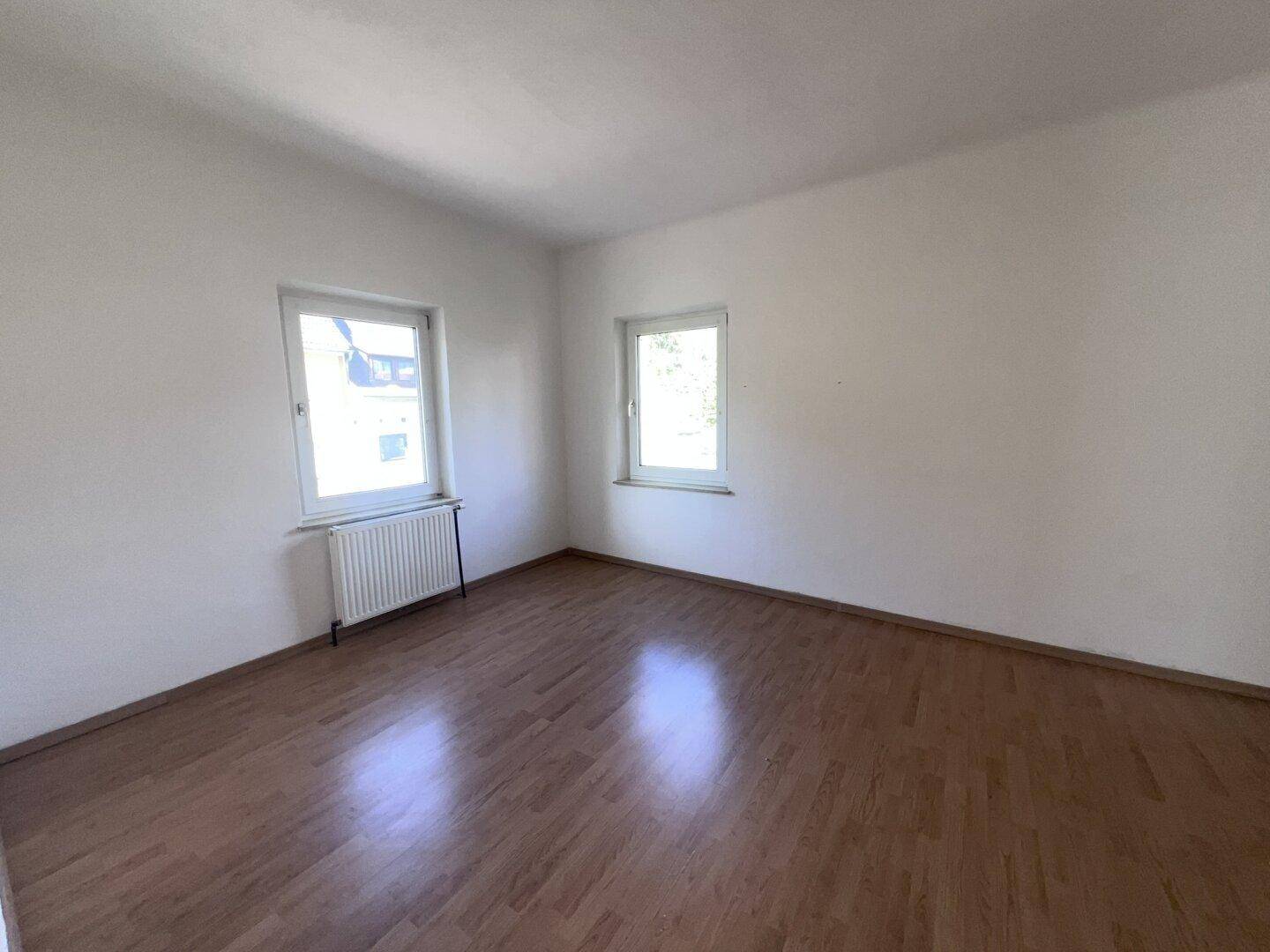 Helles Zimmer mit Laminatboden, weißen Wänden und zwei Fenstern für natürliche Belichtung.
