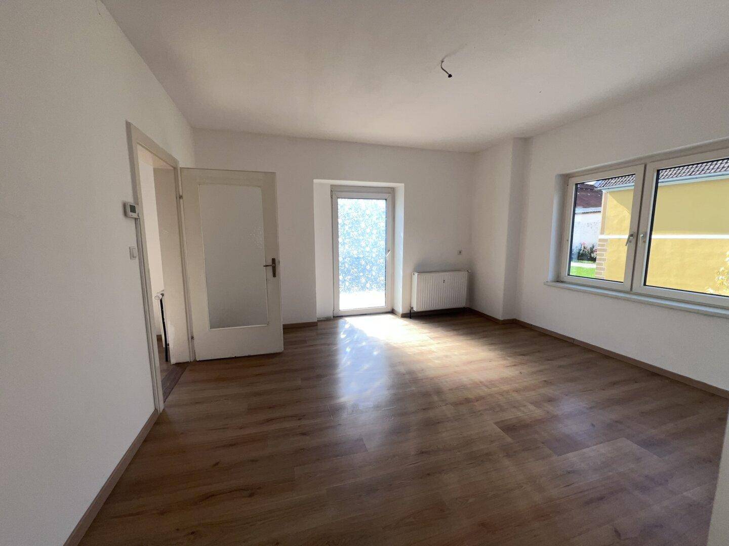 Helles Zimmer mit Laminatboden, weißen Wänden und Zugang zu einem Balkon.