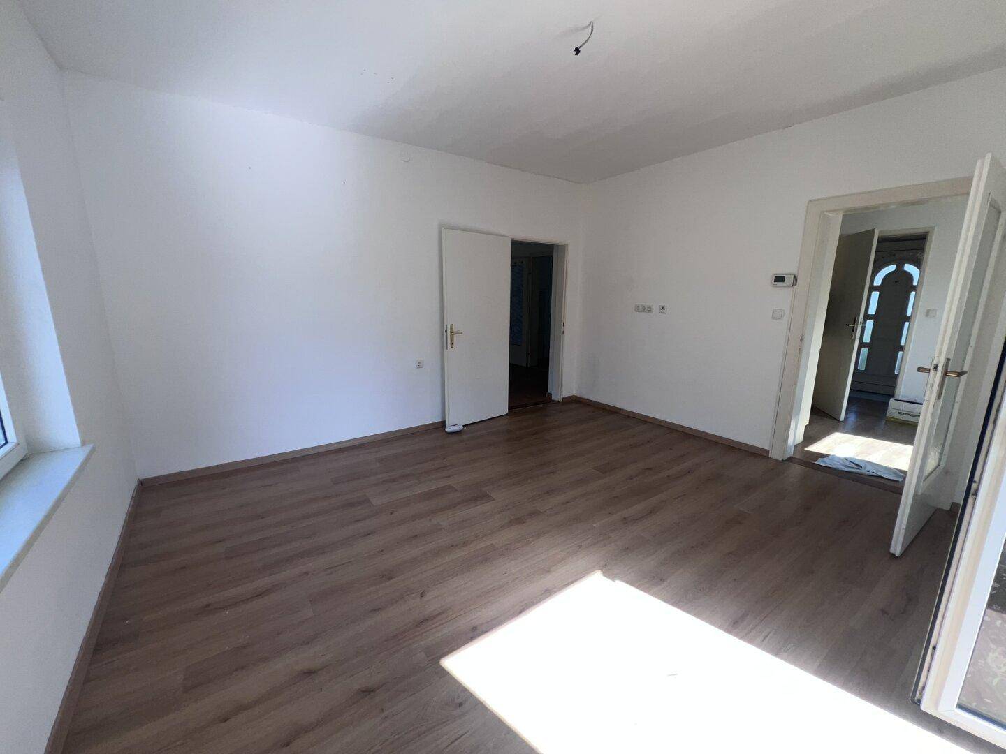 Geräumiges, helles Zimmer mit Laminatboden und Zugang zu weiteren Räumen und dem Balkon.