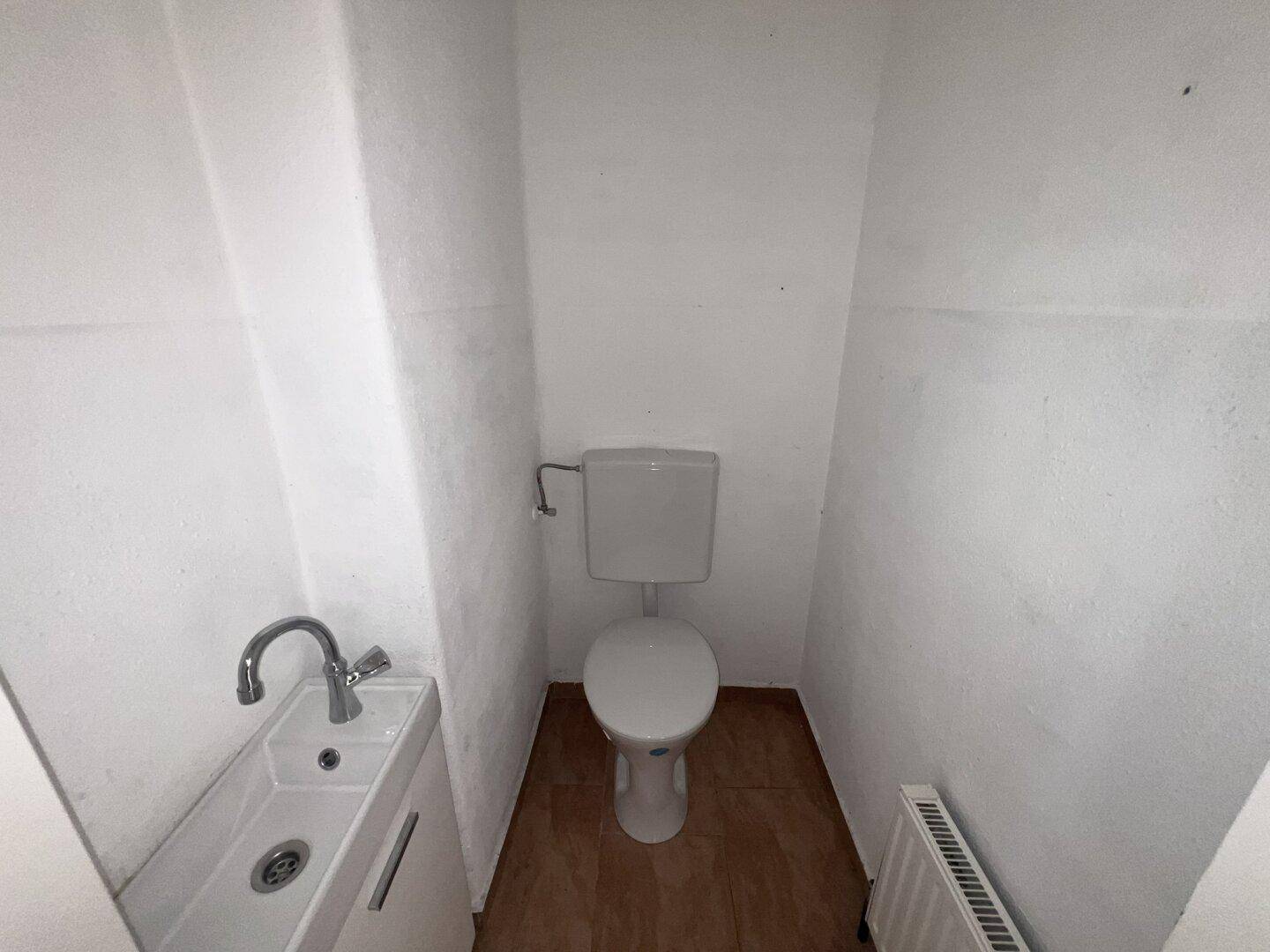 Kleines Gäste-WC mit Toilette, Handwaschbecken und Heizkörper in weißem Raum.