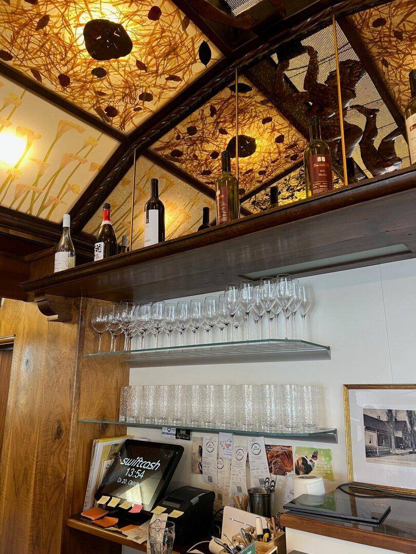 Detailansicht der Bar mit Glasregalen, Flaschen und der einzigartigen, beleuchteten Deckenverkleidung in einem Café.