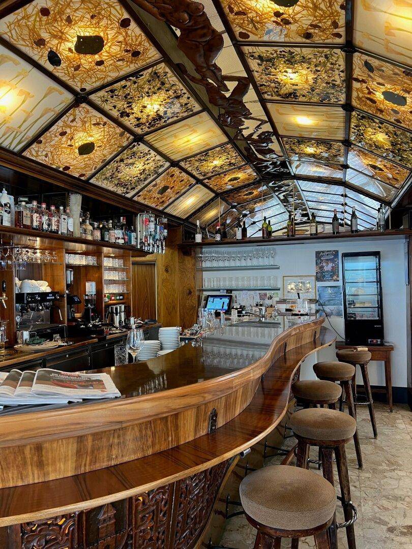 Geschwungene Holztheke mit Barhockern und einer kunstvoll gestalteten Decke in einem eleganten Café-Ambiente.