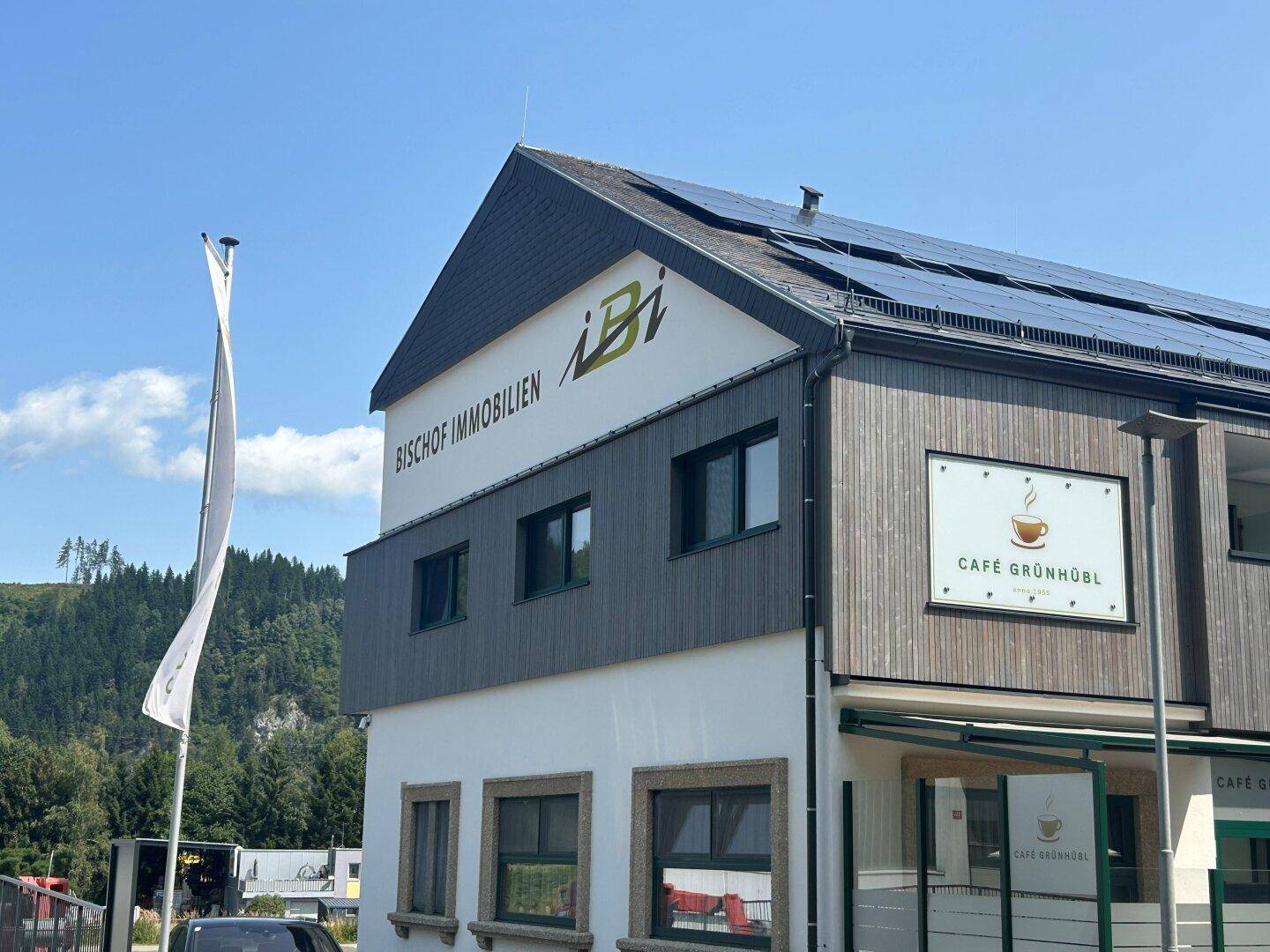 Detailansicht der modernen Gebäudefassade mit Holzverkleidung, Fenstern und Solarpaneelen auf dem Dach.
