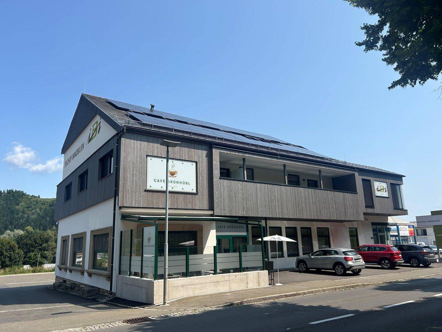 Modernes Geschäftsgebäude mit Holzfassade, großen Fenstern und Photovoltaikanlage auf dem Dach.