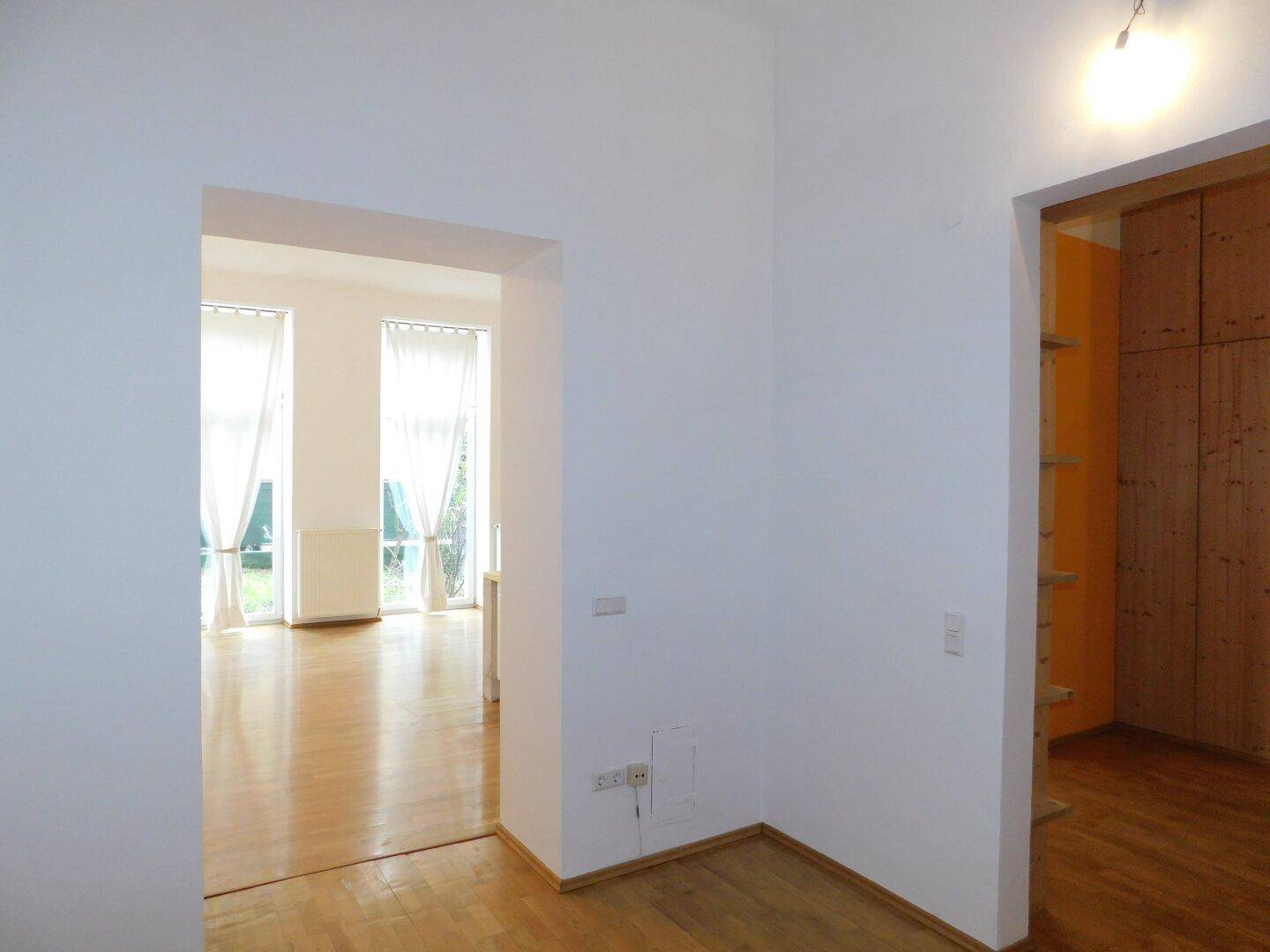 Offener Wohnbereich mit Zugang zu einem Zimmer mit Holzregalen und Blick auf die Fensterfront.