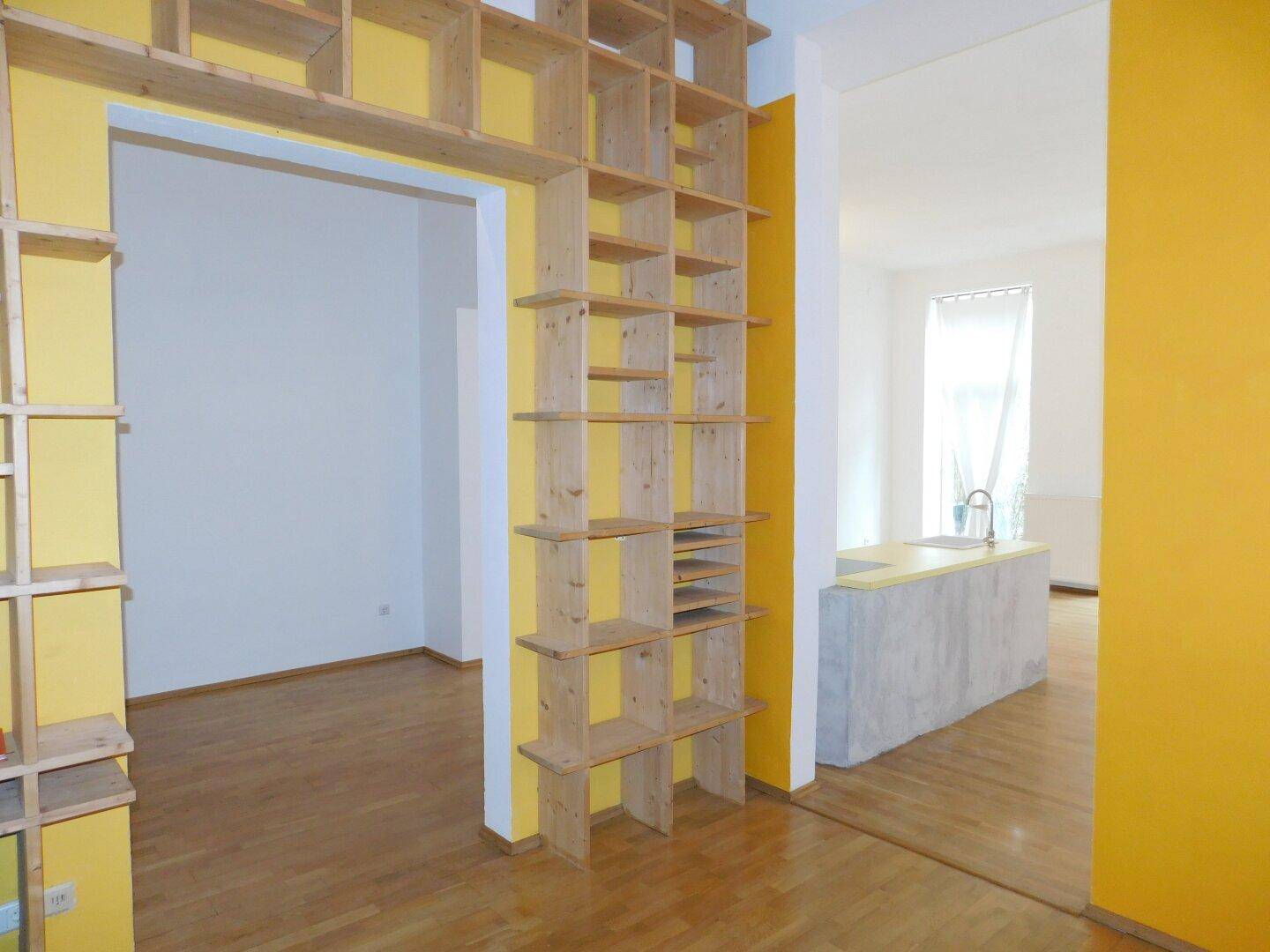 Individuell gestalteter Durchgang mit eingebauten Holzregalen und gelber Akzentwand, angrenzend an die Küche.