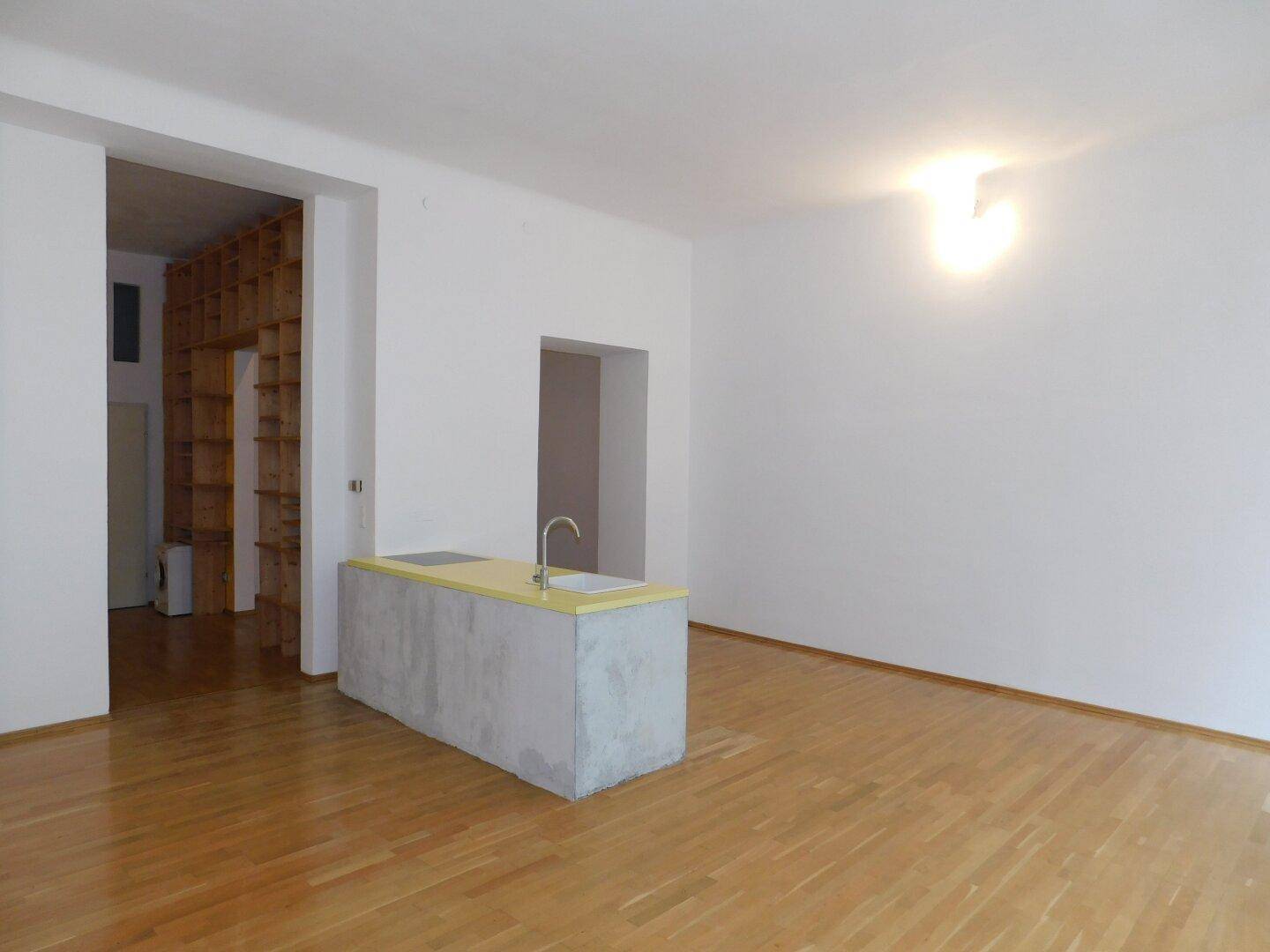 Heller Wohnraum mit Kücheninsel und Zugang zu einem Bereich mit Holzregalen.