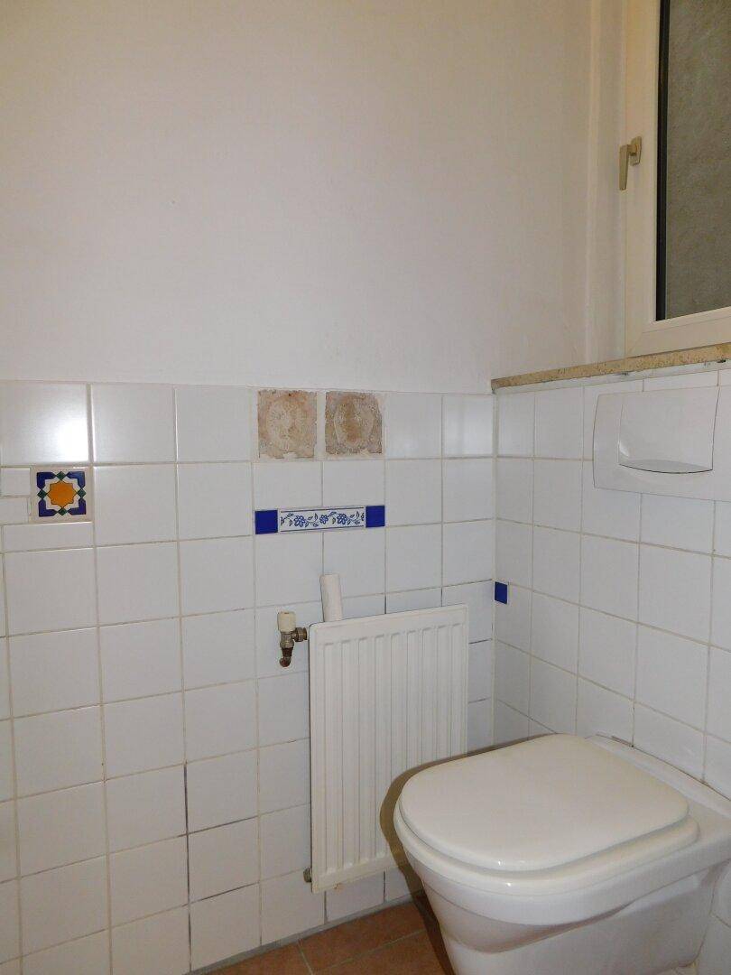 Separate Toilette mit Fenster, Wand-WC und weißen Fliesen mit blauen Akzenten, gut beleuchtet.