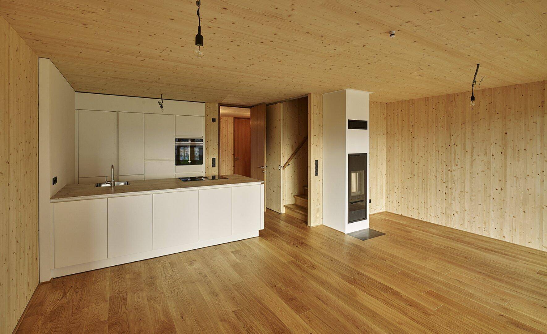 Heller offener Wohnbereich mit moderner Einbauküche, Holzböden und Kamin.