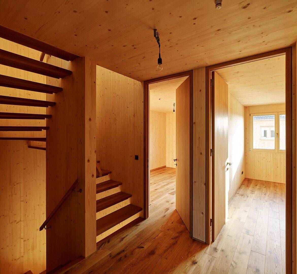 Heller Flur mit Holzvertäfelung, Holzboden und offener Holztreppe, die zu weiteren Räumen führt.