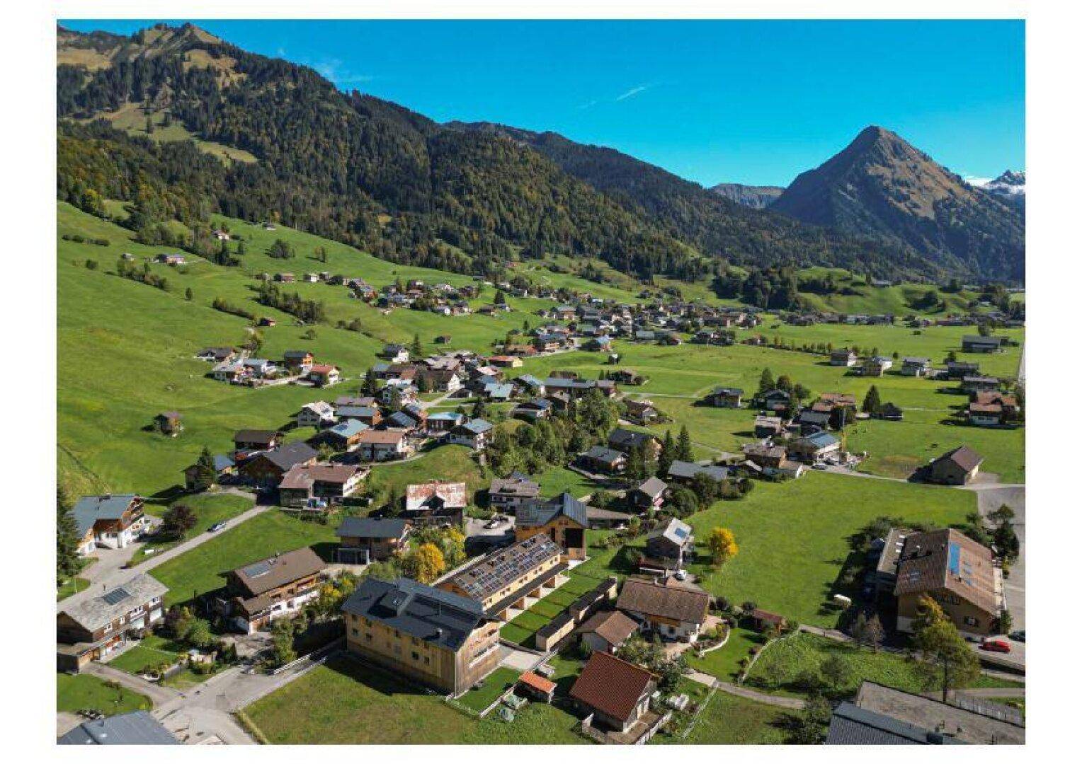 Luftaufnahme eines malerischen Dorfes in einem grünen Tal, umgeben von majestätischen Bergen.