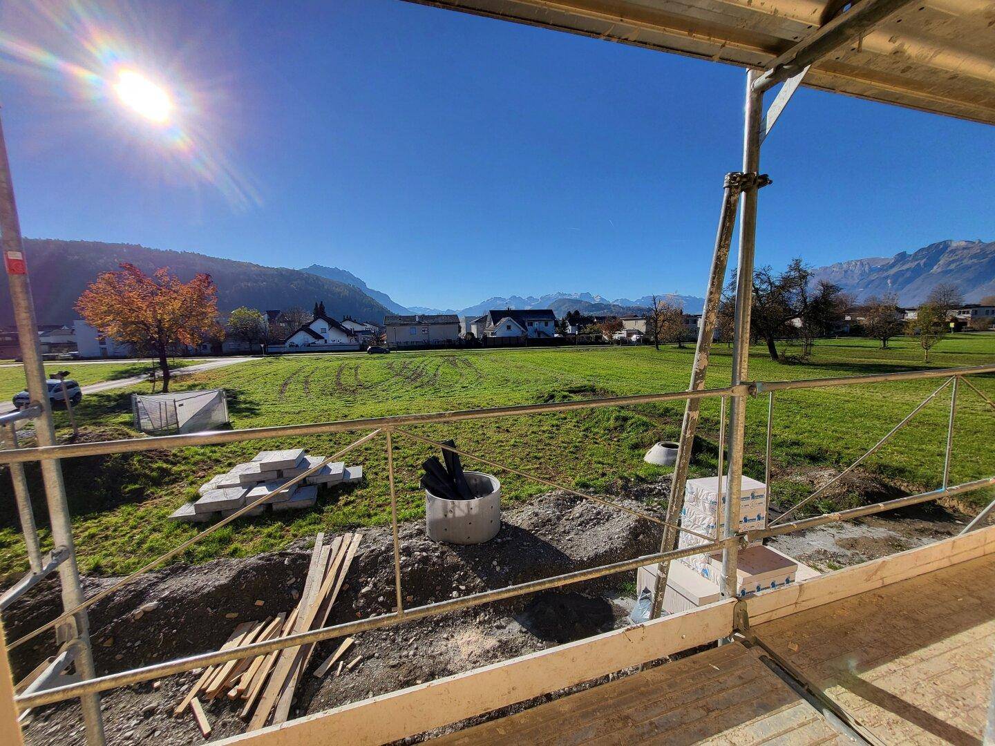 Blick von einer Baustelle über grüne Felder auf eine Berglandschaft und umliegende Häuser.