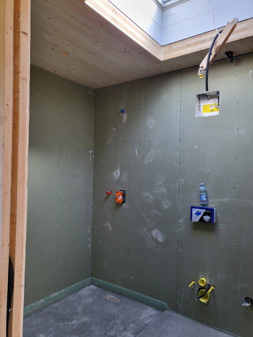 Badezimmer im Rohbau mit sichtbaren Installationen, grünen Trockenbauwänden und einem Oberlicht.