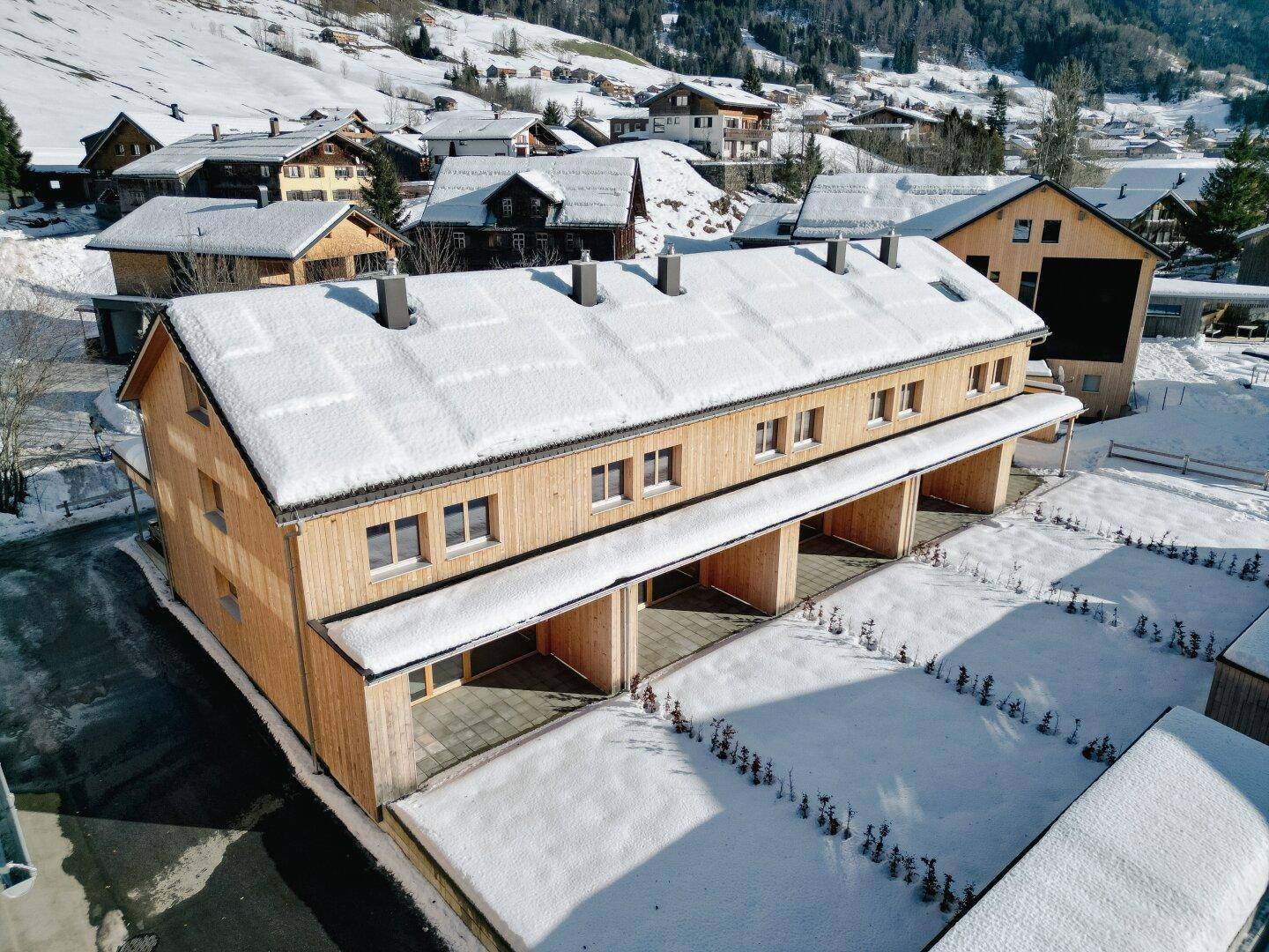Luftaufnahme der neuen Reihenhäuser mit Holzfassade, umgeben von verschneiter Landschaft.
