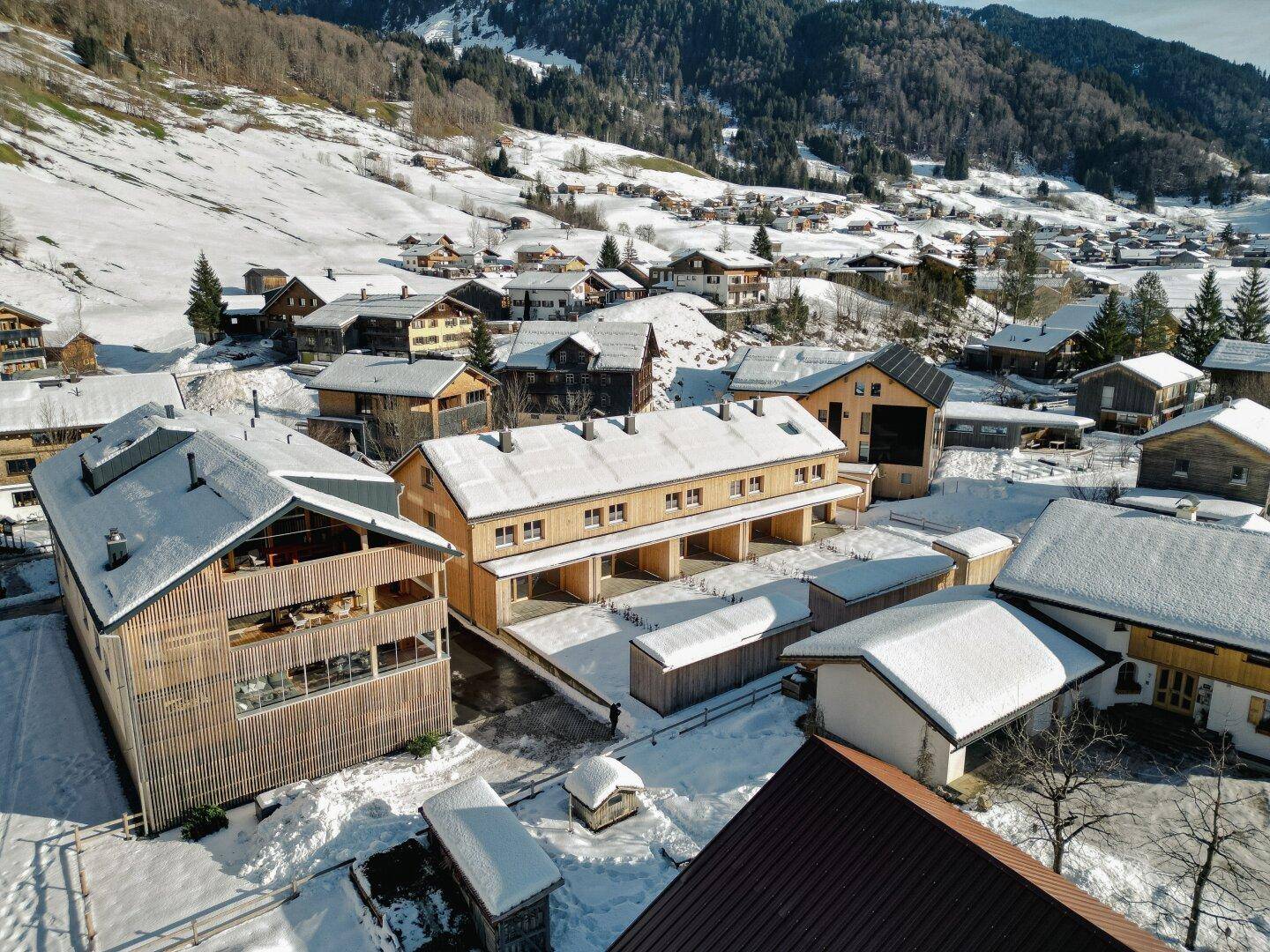 Weitläufige Luftaufnahme der Reihenhäuser in einer verschneiten Berglandschaft mit Dorfbebauung.