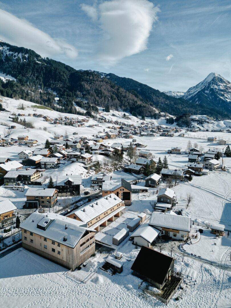 Panoramablick auf ein verschneites Bergdorf mit umliegenden schneebedeckten Bergen und Tälern.