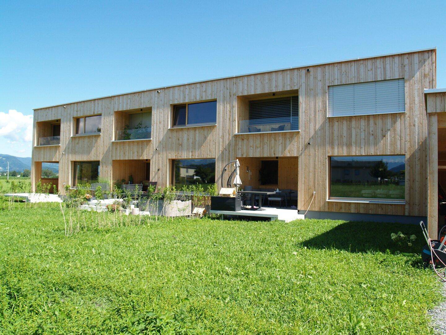 Rückseite des Holzhauses mit mehreren Terrassen und Sitzgelegenheiten im Gartenbereich.
