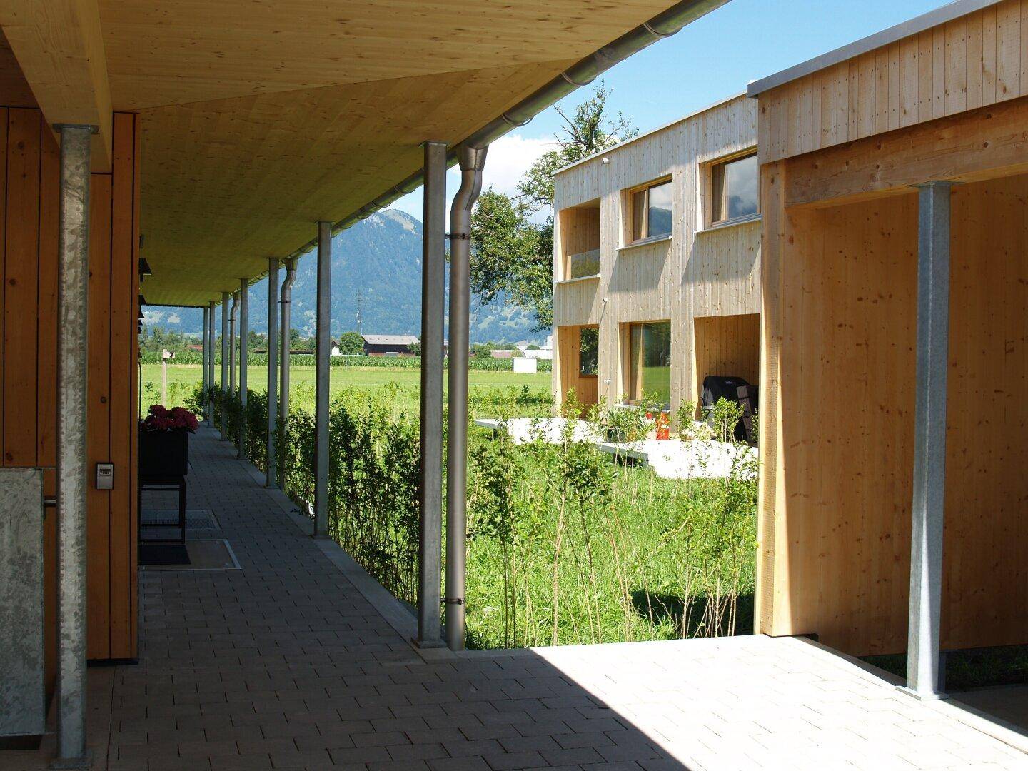 Überdachter Gang mit Holzdach und Blick auf die umliegende Landschaft und Berge.