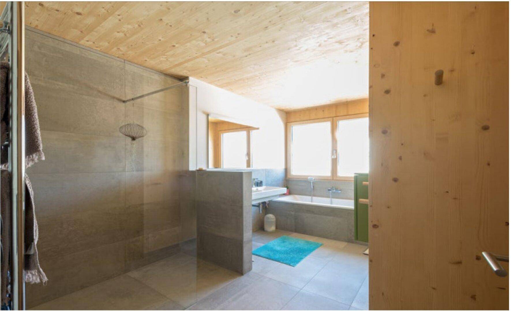 Modernes Badezimmer mit begehbarer Dusche, Badewanne, Holzdecke und hellen Fliesen.