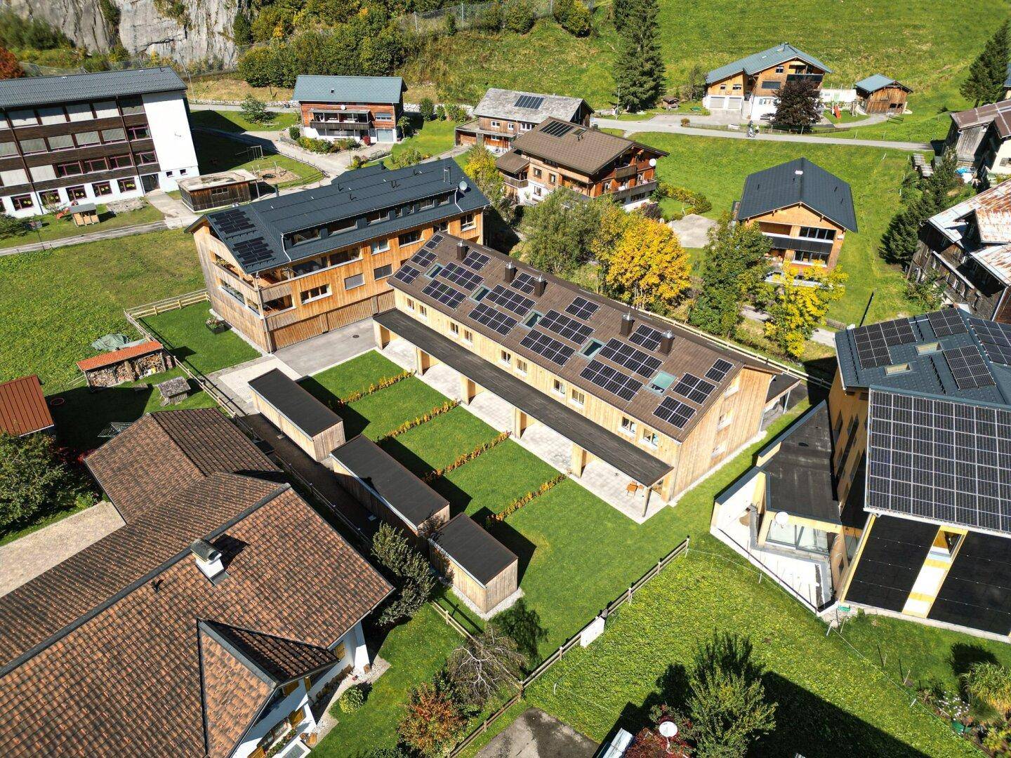 Vogelperspektive auf eine Gruppe von Gebäuden mit Solaranlagen auf den Dächern, eingebettet in grüne Wiesen.