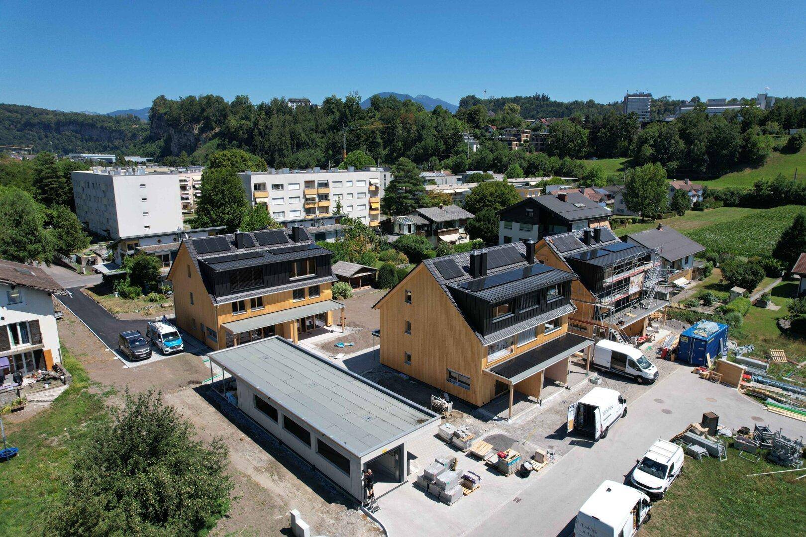 Luftaufnahme von modernen Holzhäusern im Bau mit Photovoltaikanlagen auf den Dächern.