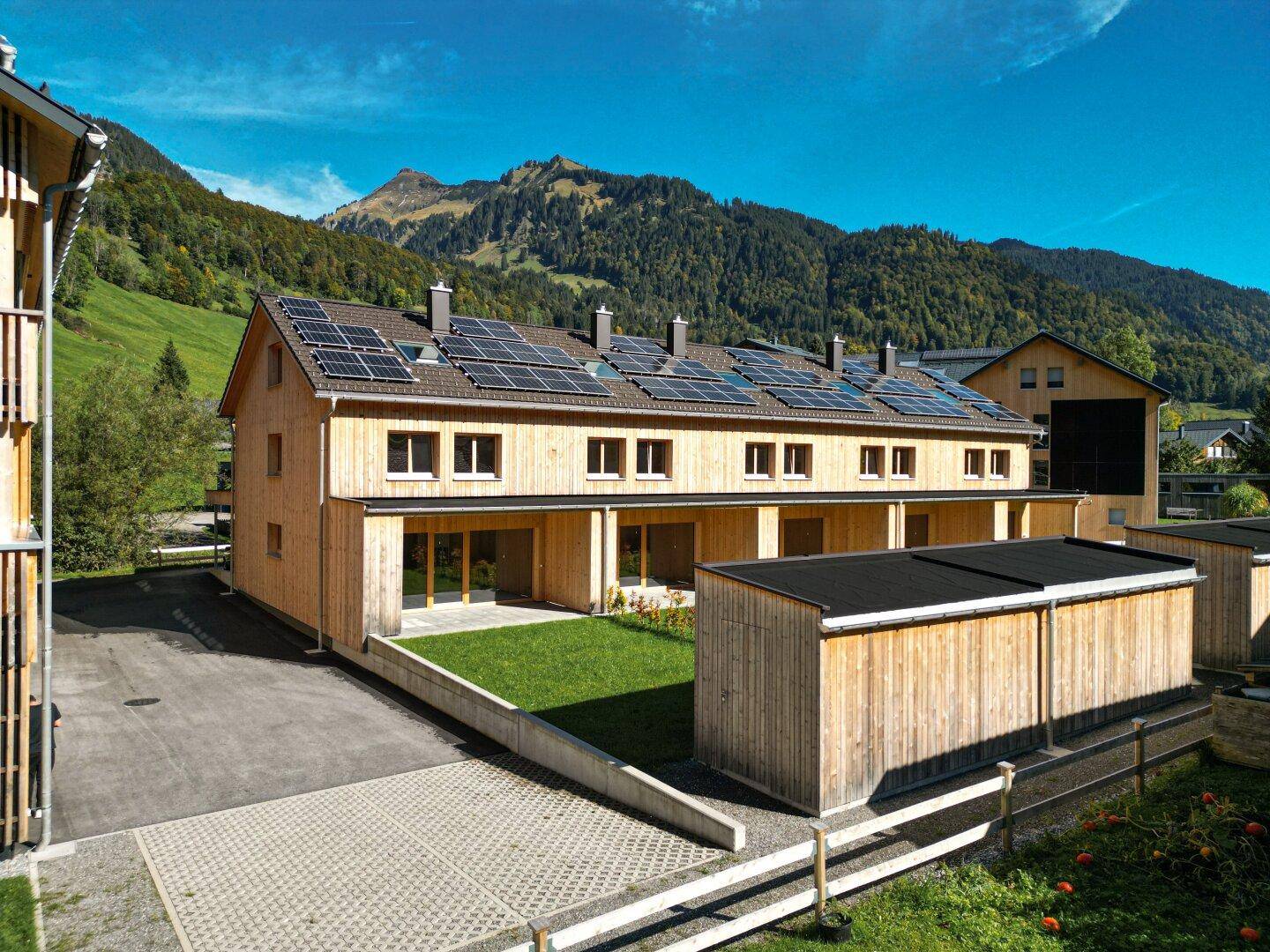 Moderne Reihenhäuser aus Holz mit Solaranlagen auf dem Dach und Bergblick in sonniger Lage.