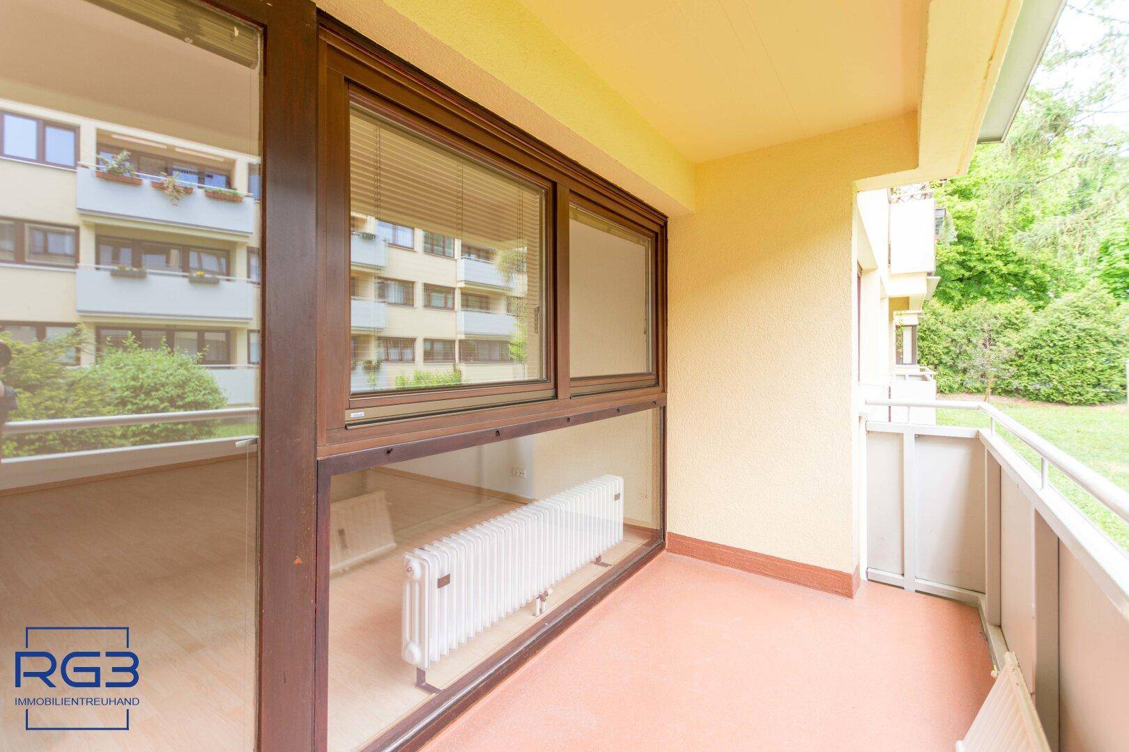 Heller Balkon mit Fliesenboden und Blick auf die umliegenden Gebäude und Bäume.