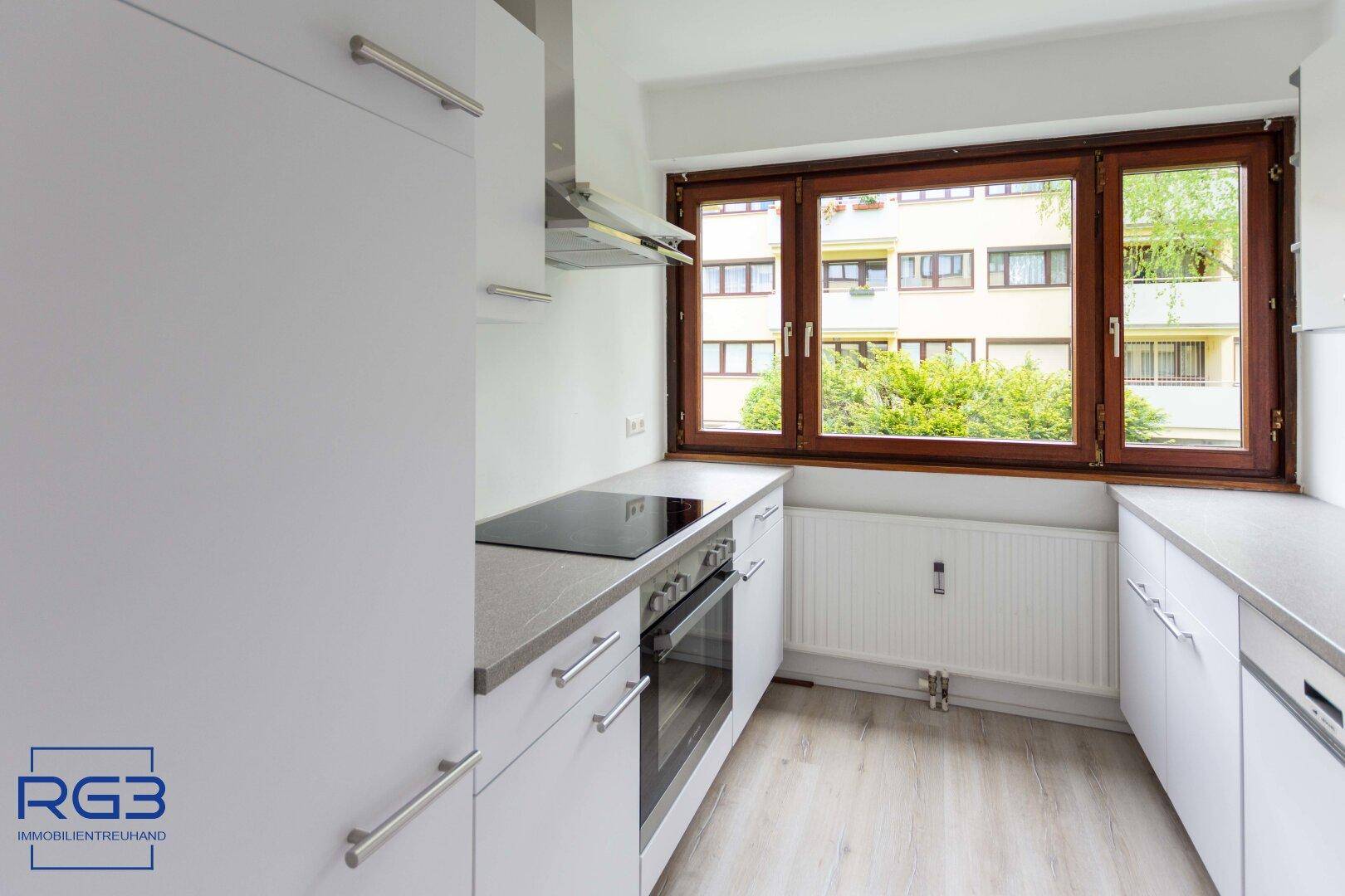 Funktionale Küche mit weißen Schränken, modernen Geräten und Fenster mit Ausblick.