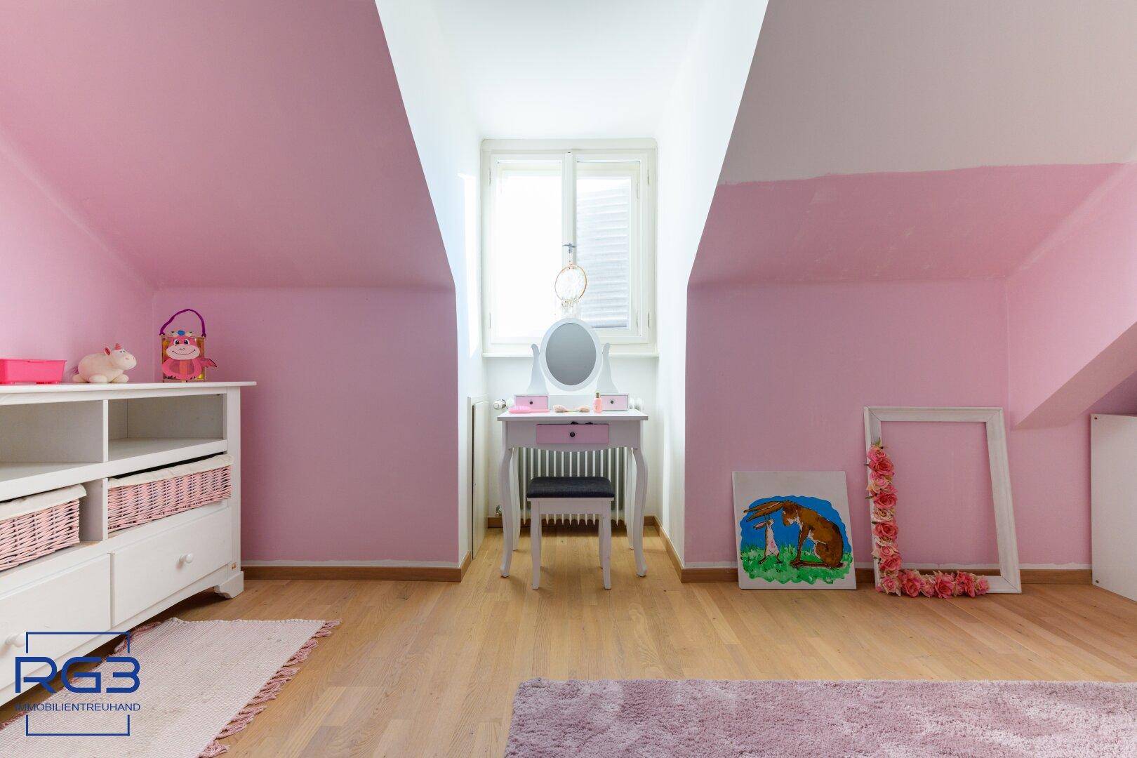 Mädchenzimmer im Dachgeschoss mit rosa Wänden, Holzboden und Schminktisch.