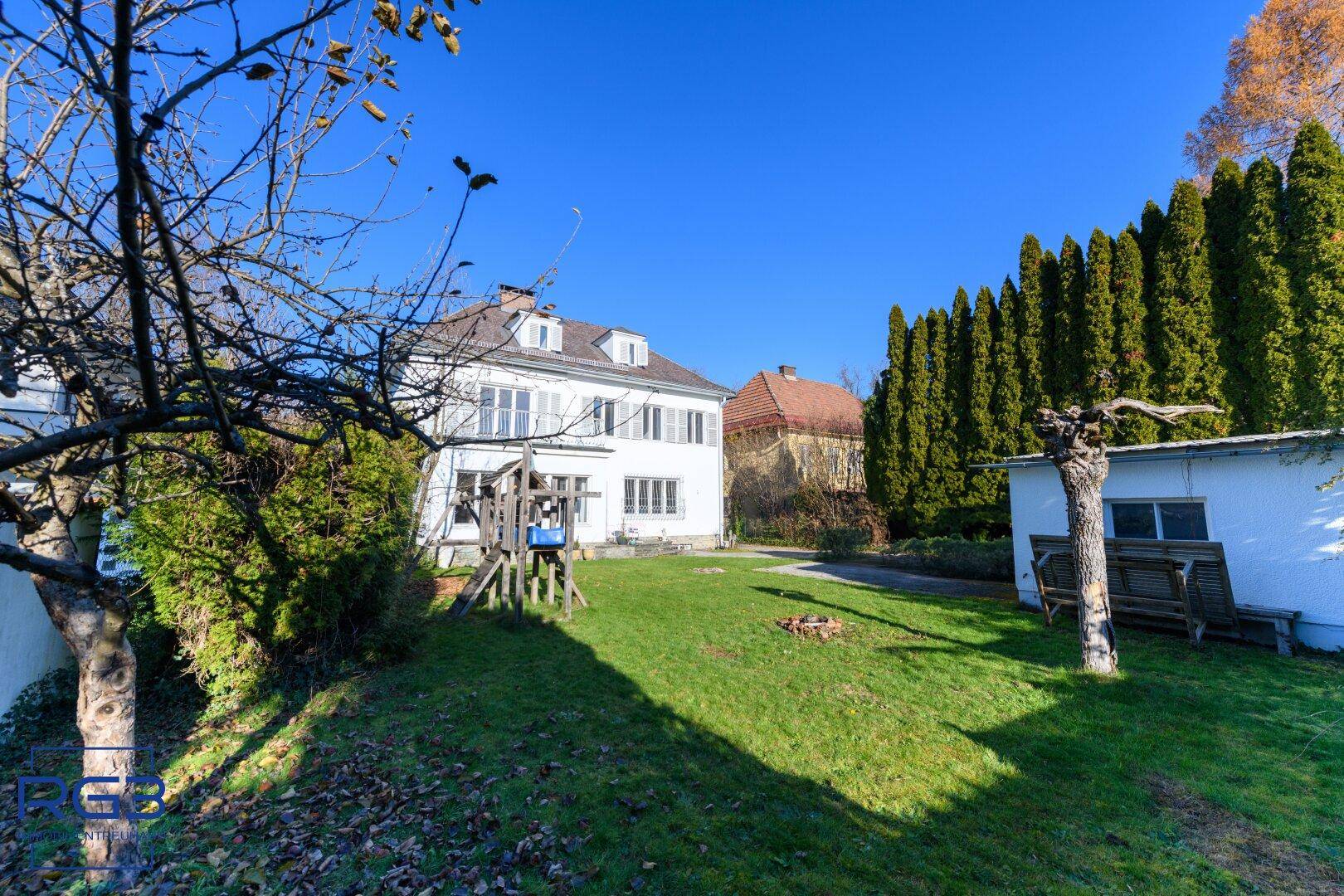 Großer, gepflegter Garten mit Rasenfläche, hohen Hecken und einem Spielgerät im Freien.