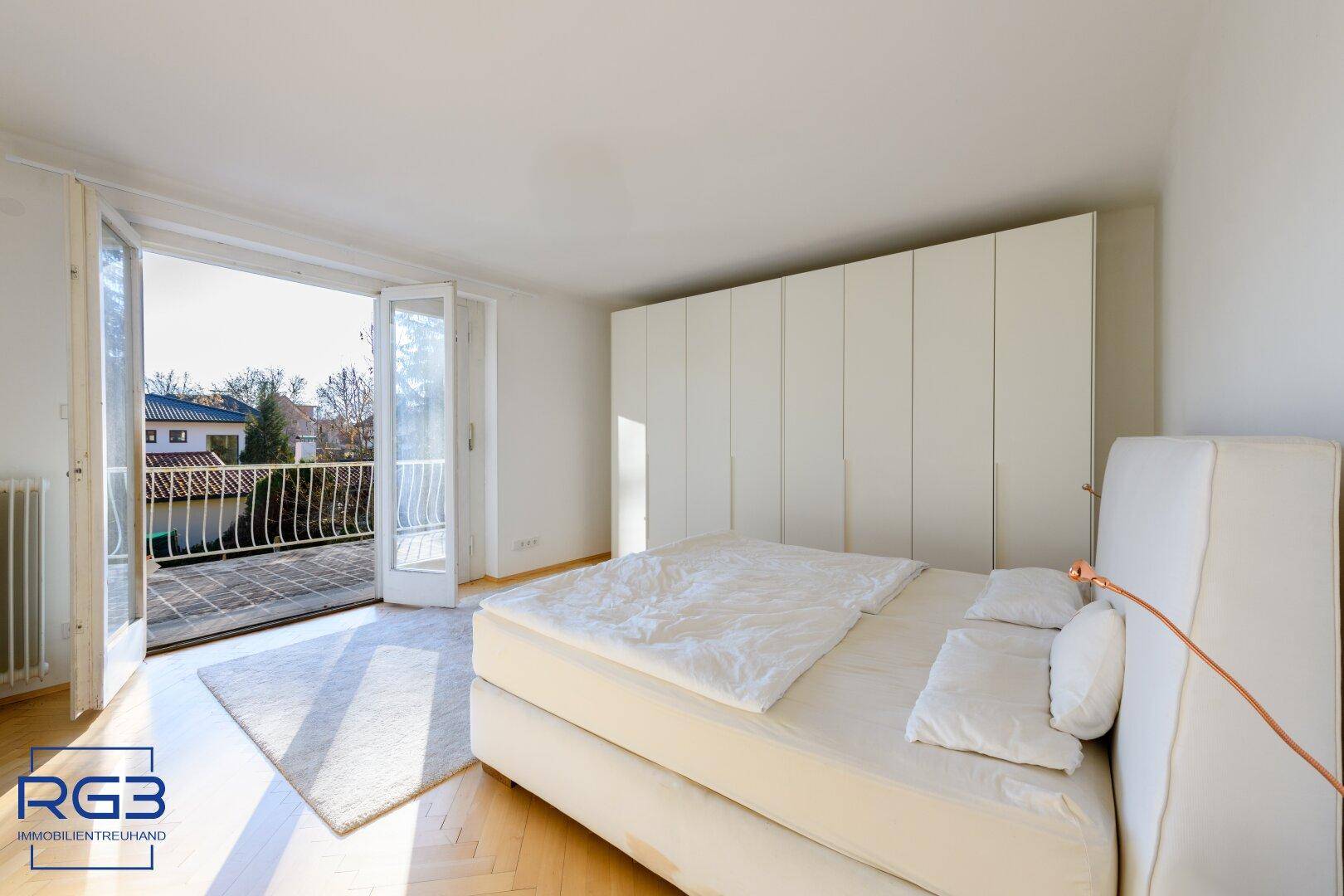 Helles Schlafzimmer mit Doppelbett, Einbauschränken und Zugang zum Balkon.